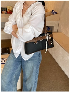 Détail du sac cabas noir minimaliste avec boucle en cuir marron et pendentifs tressés
