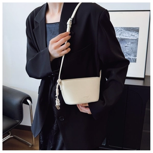 Close-up of minimalist cream crossbody bag in litchi grain leather on a black blazer