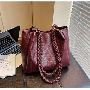 Close-up of woven wine red leather tote bag with gold lettering in a home office setting
