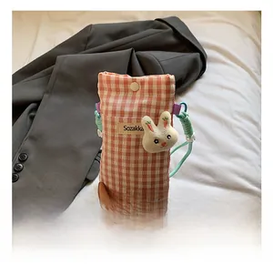 Détail d'un sac de téléphone à carreaux avec lapin en peluche et bandoulière en corde