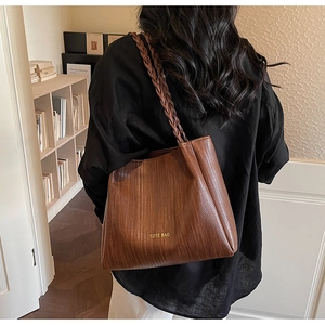 Detail of a brown woven tote bag with braided straps and TOTE BAG lettering print