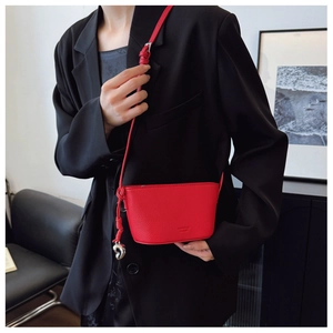 Close-up of a red leather mini crossbody bag with a heart pendant on a black blazer