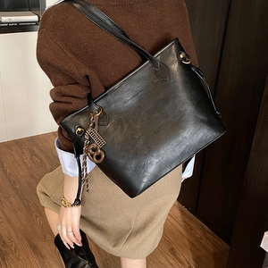 Close-up of black leather tote bag featuring an embossed logo and wooden bow charm