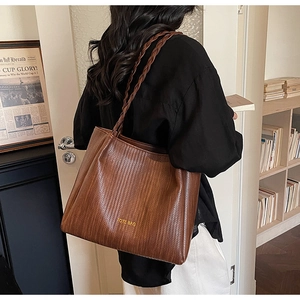 Brown woven leather tote bag shown on shoulder in a stylish minimalist interior setting