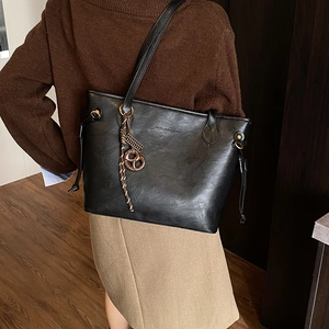 Detail shot of the matte black faux leather tote bag with woven pendant and metal ring charm