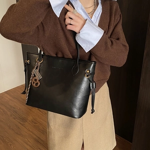 Detail of black faux leather tote bag featuring drawstring sides and woven handle pendant