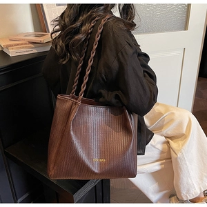 Detail view of woven brown tote bag with gold lettering on a model for daily commute
