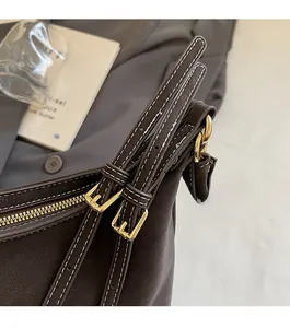 Détail du sac en cuir marron foncé avec coutures blanches et boucle en métal doré