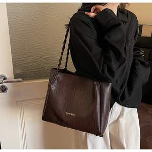 Detail of dark brown tote bag featuring woven texture and stylish woven shoulder strap