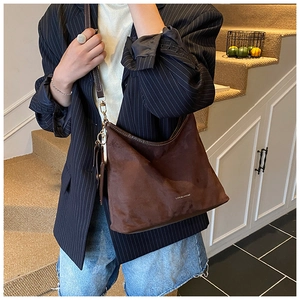 Detail of a large dark brown suede tote bag featuring a minimalist metal logo on front