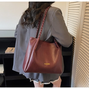 Detail of burgundy woven tote bag with yellow lettering carried by model over the shoulder