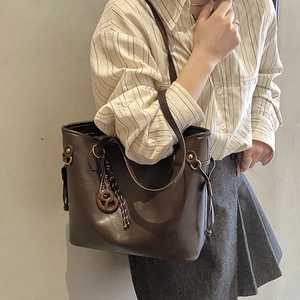 Detail of dark brown faux leather tote bag with wooden charm and woven rope decoration