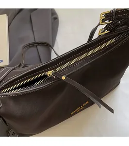 Détail du sac en cuir marron foncé avec fermeture éclair dorée et logo en lettres