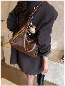 Dettaglio borsa hobo in vernice marrone scuro con tracolla annodata e ciondoli peluche