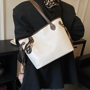Detailed close-up of creamy white faux leather tote bag with brown straps and woven charm