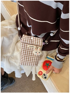 Détail du sac à bandoulière à carreaux marron avec lapin en peluche et étiquette