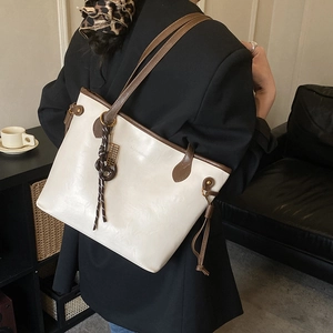 Detail of minimalist cream tote bag with brown trim and tassel decoration on a model