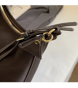 Gros plan du sac en cuir marron avec coutures contrastées et pendentif triangle doré