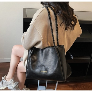 Detail of black woven texture tote bag with braided shoulder strap and gold lettering