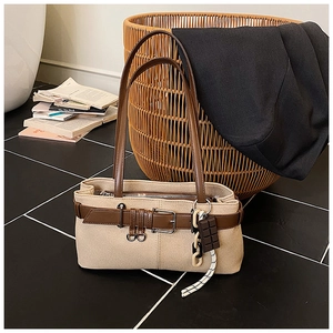Détail d'un sac cabas en toile beige avec lanière en cuir brun et breloque chocolat