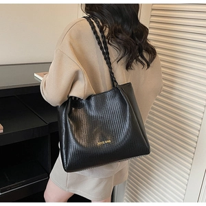 Detail of black woven tote bag with gold lettering and braided straps on shoulder