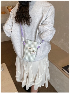 Détail d'un sac à téléphone à carreaux avec breloque lapin et bandoulière tissée mauve