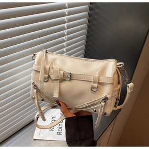 Close-up of cream crossbody bag with silver zippers, metal rivets and punk style details