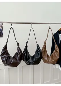 Trois sacs demi-lune en marron foncé, noir et camel suspendus sur une barre d'affichage