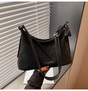Détail du sac bandoulière en daim noir avec coutures contrastées blanches et logo doré