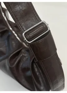 Détail de la bandoulière réglable avec boucle argentée sur un sac en cuir marron