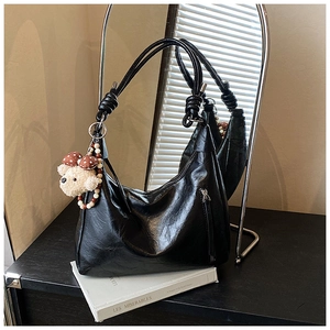 Dettaglio borsa hobo in pelle nera opaca con tracolla a nodo e ciondolo orsetto