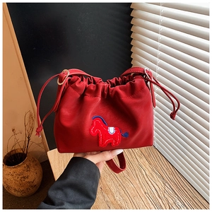 Detail of red drawstring bucket bag featuring a textured pony patch and adjustable strap