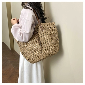 Detail of handwoven straw tote bag with brown leather straps shown on shoulder
