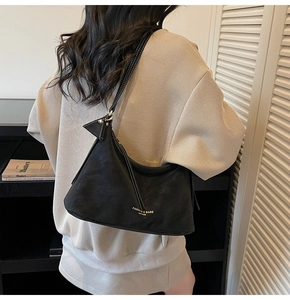 Détail du sac hobo minimaliste en cuir noir avec logo doré et pompon triangulaire