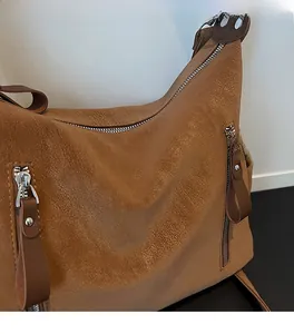 Détail de la texture cuir marron et fermetures éclair argentées d'un grand sac bandoulière