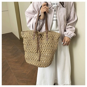 Close-up of woven straw tote bag featuring brown leather handles and drawstring closure