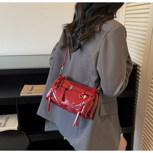 Detail of red patent leather shoulder bag with punk style zippers and metal buckles