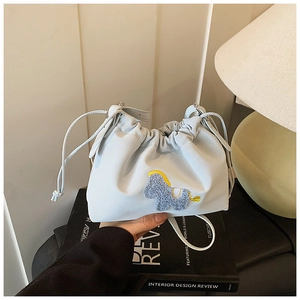 Detail of light blue drawstring bucket bag with a plush pony patch and leather strap