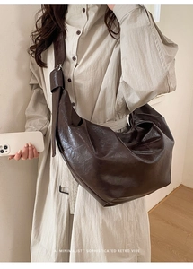 Détail du sac hobo en cuir marron foncé avec une large bandoulière décorative nouée