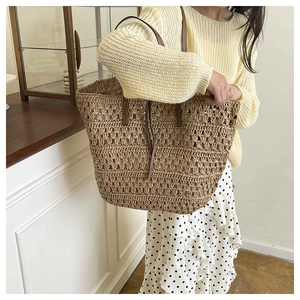 Detail of woven straw tote bag featuring brown leather straps and hollow mesh texture