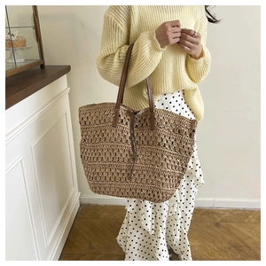 Detail view of woven straw tote bag with brown leather straps and drawstring closure