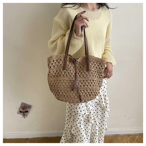 Detail of hand-woven straw tote bag with brown leather handles and stitching