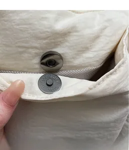 Close-up of the metal magnetic clasp and wrinkled nylon texture on a cream bucket bag