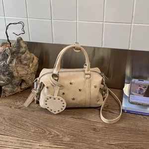 Details von sternförmigen Metallnieten und Herzanhänger an einer beigen Boston Bag