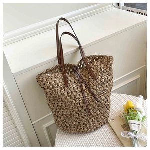 Close-up of woven straw tote bag with brown leather handles and drawstring detail