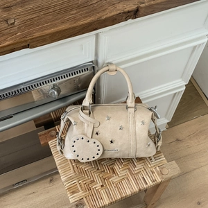 Detailansicht der beigen Vintage-Tasche mit silbernen Sternnieten und Herzanhänger