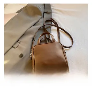 Detail view of brown leather Boston bag with handles and crossbody strap on a grey suit
