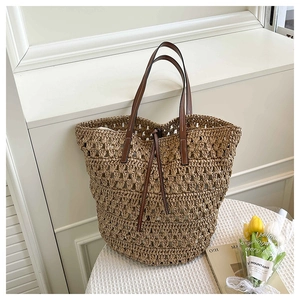 Detail of hand-woven straw tote bag with brown leather handles and drawstring closure