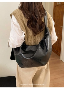 Détail d'un grand sac hobo en cuir noir brillant avec texture rétro sur un mannequin