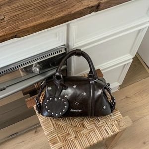 Detailansicht der braunen Leder-Bostontasche mit silbernen Sternnieten auf einem Stuhl